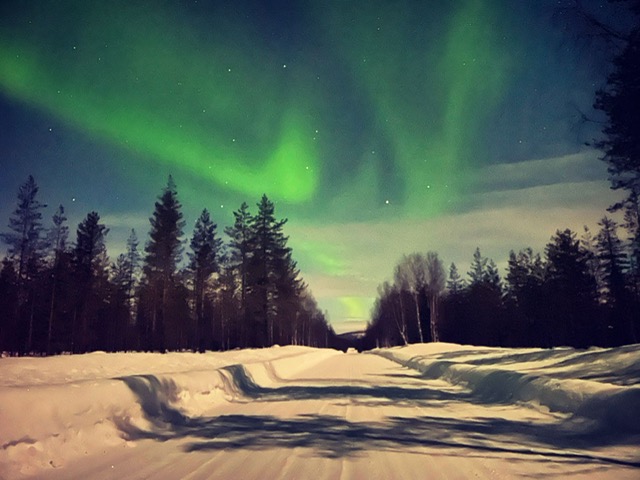 Beautiful northern lights giving magical light for the road to Villa Vasa in Rovaniemi